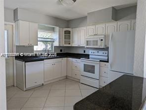 kitchen featuring light tile patterned floors, white appliances, white cabinetry, and dark countertops