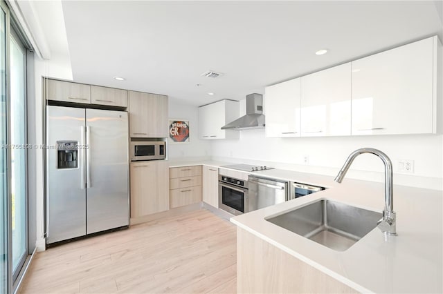 kitchen featuring visible vents, a sink, appliances with stainless steel finishes, wall chimney range hood, and modern cabinets