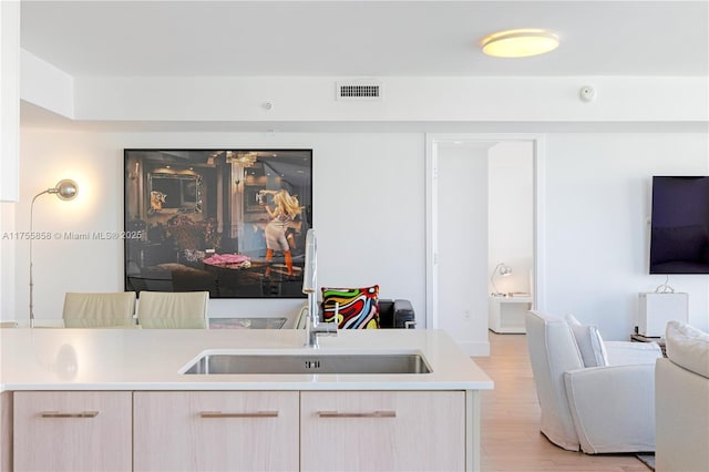 kitchen with visible vents, light brown cabinetry, a sink, open floor plan, and light wood-style floors