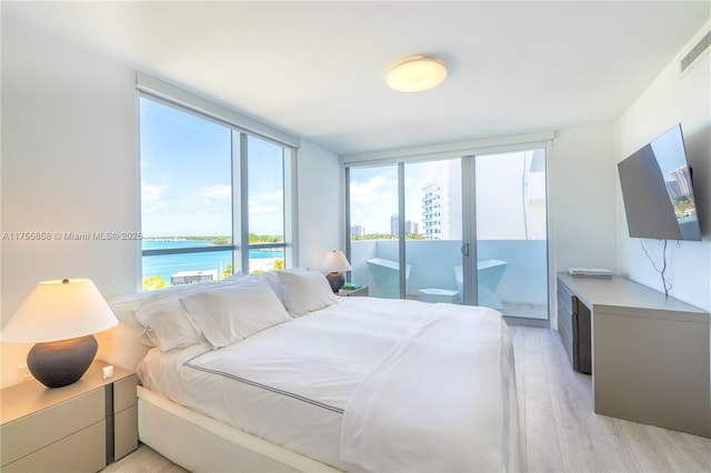 bedroom featuring visible vents, light wood finished floors, a water view, and access to outside