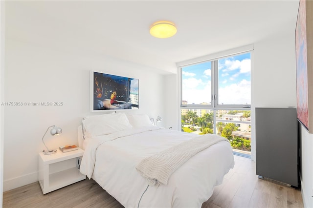 bedroom featuring baseboards, light wood-style floors, and expansive windows