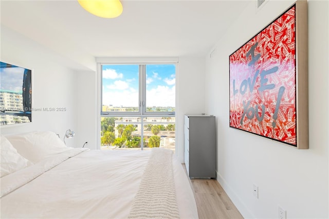 bedroom with expansive windows, a view of city, baseboards, and wood finished floors