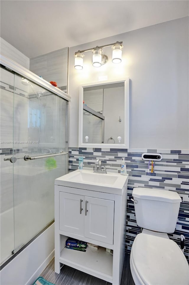 bathroom with combined bath / shower with glass door, toilet, tile walls, and vanity