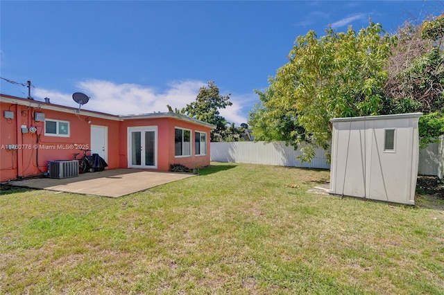 view of yard featuring an outbuilding, a patio, central AC, a fenced backyard, and french doors