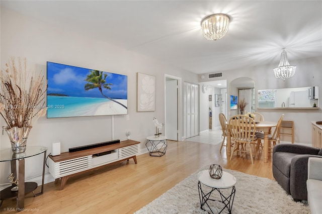 living area with visible vents, wood finished floors, arched walkways, and a chandelier