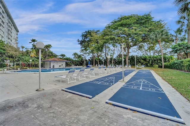 view of community featuring a swimming pool, fence, shuffleboard, and a patio area