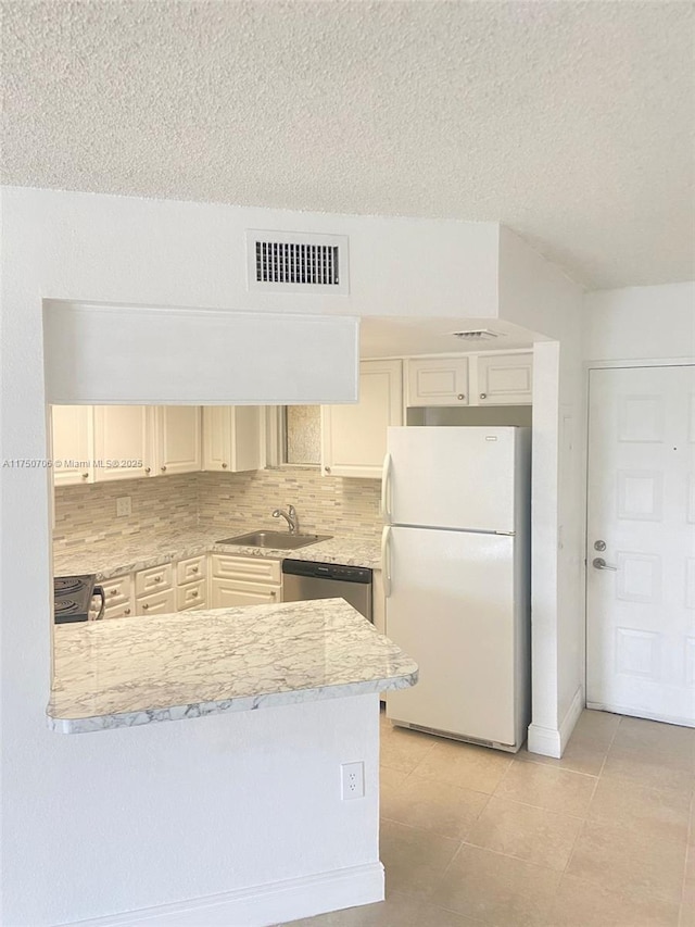 kitchen featuring tasteful backsplash, visible vents, a peninsula, freestanding refrigerator, and a sink