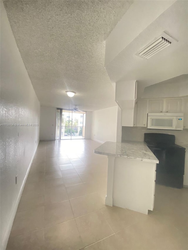 interior space featuring light tile patterned floors, white microwave, visible vents, white cabinetry, and open floor plan