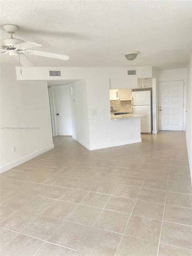 spare room with light tile patterned floors, visible vents, a textured ceiling, and a ceiling fan