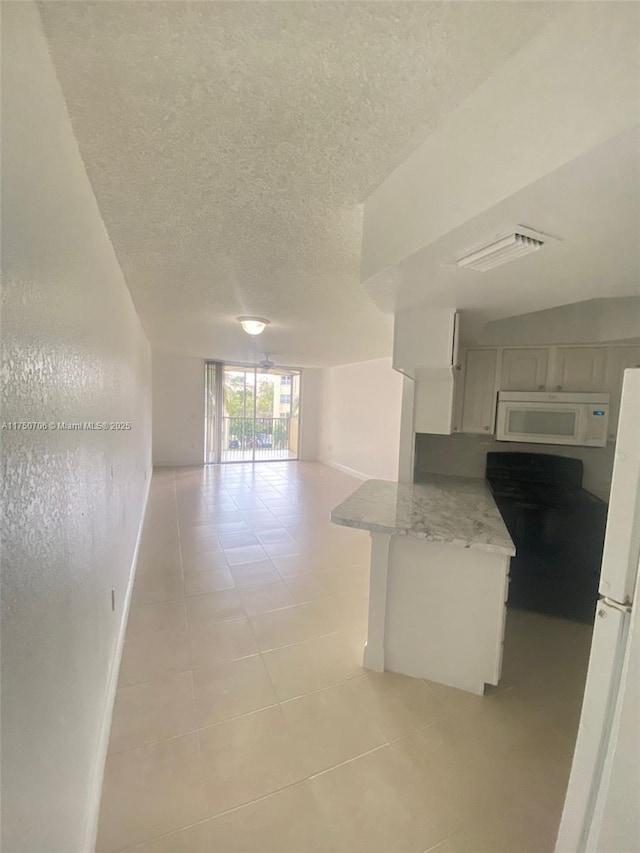 kitchen featuring a textured ceiling, open floor plan, white appliances, light countertops, and light tile patterned floors