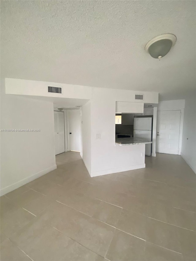 unfurnished room with tile patterned floors, baseboards, visible vents, and a textured ceiling