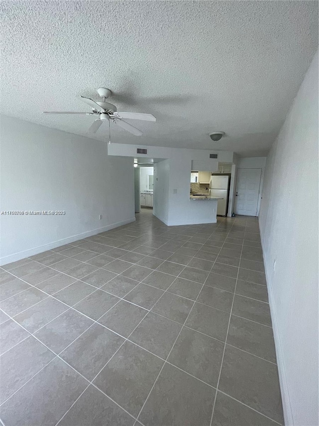 unfurnished living room featuring baseboards, a textured ceiling, ceiling fan, and dark tile patterned flooring