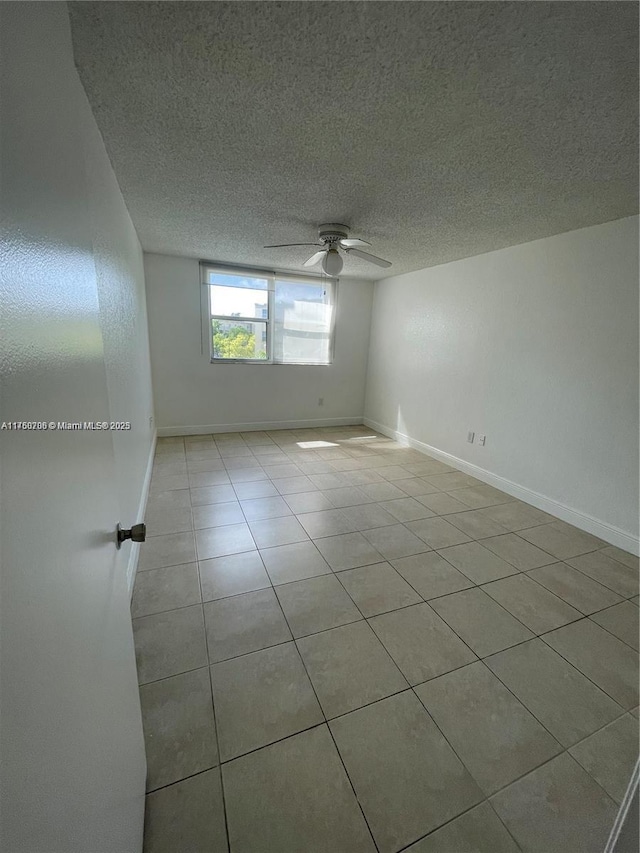 empty room with baseboards, tile patterned floors, a textured ceiling, and a ceiling fan