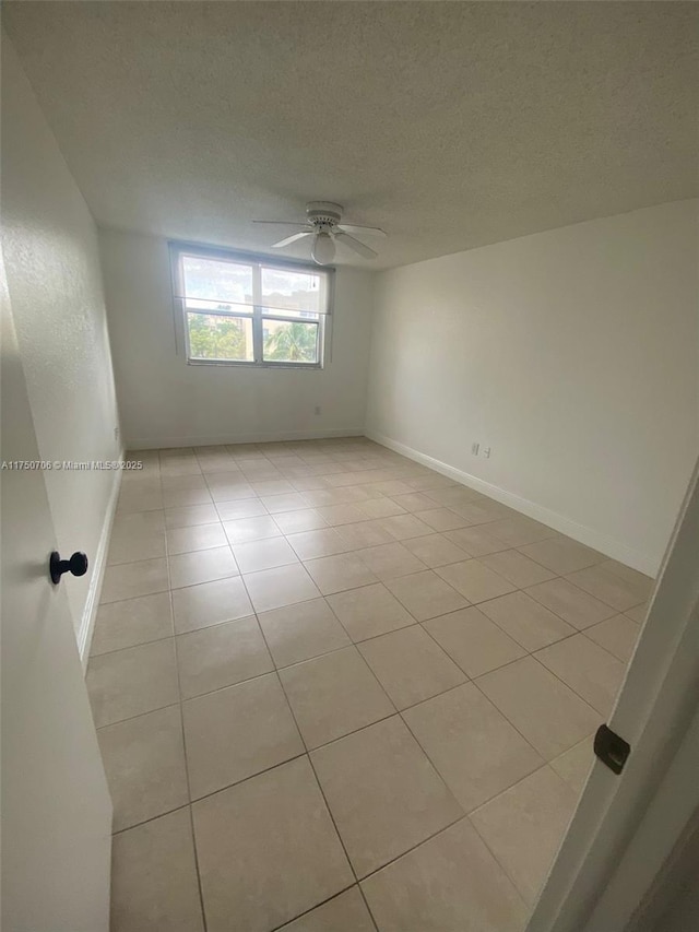 spare room featuring baseboards, a textured ceiling, light tile patterned flooring, and a ceiling fan