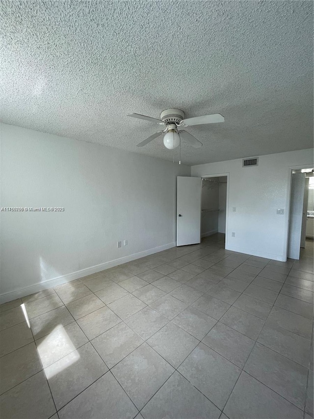 spare room with tile patterned flooring, visible vents, baseboards, ceiling fan, and a textured ceiling