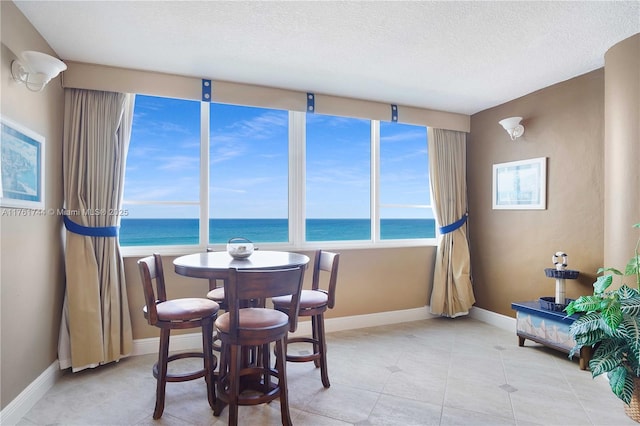 dining area featuring light tile patterned flooring, a textured ceiling, baseboards, and a water view