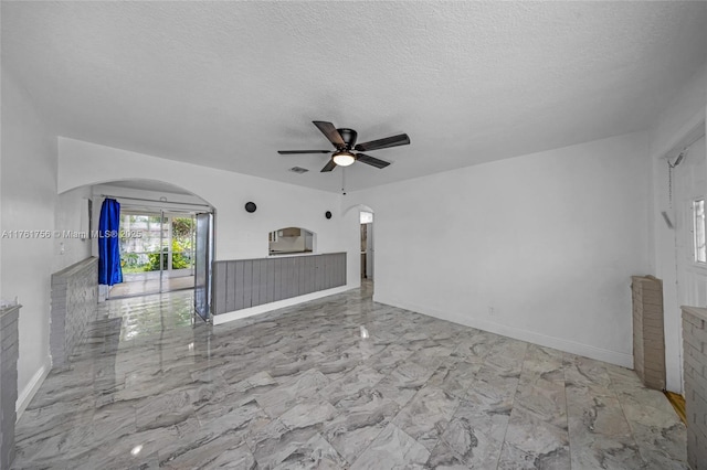 unfurnished living room featuring marble finish floor, a ceiling fan, a textured ceiling, arched walkways, and baseboards