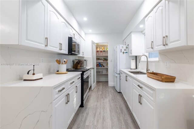 kitchen featuring light wood-style flooring, a sink, tasteful backsplash, white cabinetry, and appliances with stainless steel finishes