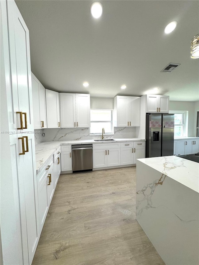 kitchen with visible vents, light stone counters, appliances with stainless steel finishes, white cabinetry, and a sink