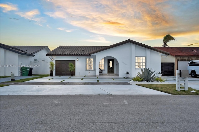 view of front of property with fence, driveway, stucco siding, a garage, and a tile roof