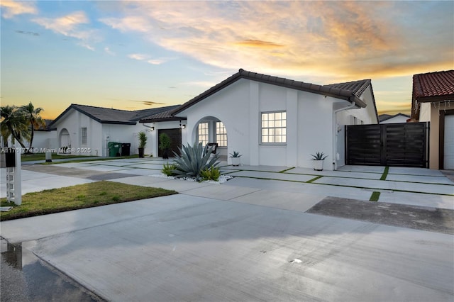 view of front of home with a tile roof, concrete driveway, stucco siding, an attached garage, and a gate