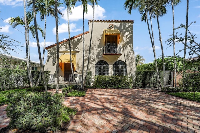 view of front facade with a tile roof, a balcony, fence, and stucco siding