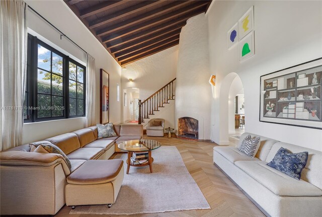 living room with beamed ceiling, arched walkways, a high ceiling, and stairs