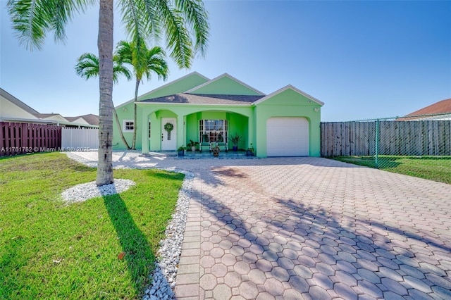 view of front of house featuring an attached garage, fence, a front lawn, and decorative driveway