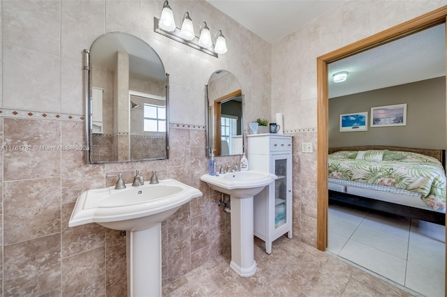 ensuite bathroom with ensuite bathroom, a sink, tile patterned flooring, and tile walls