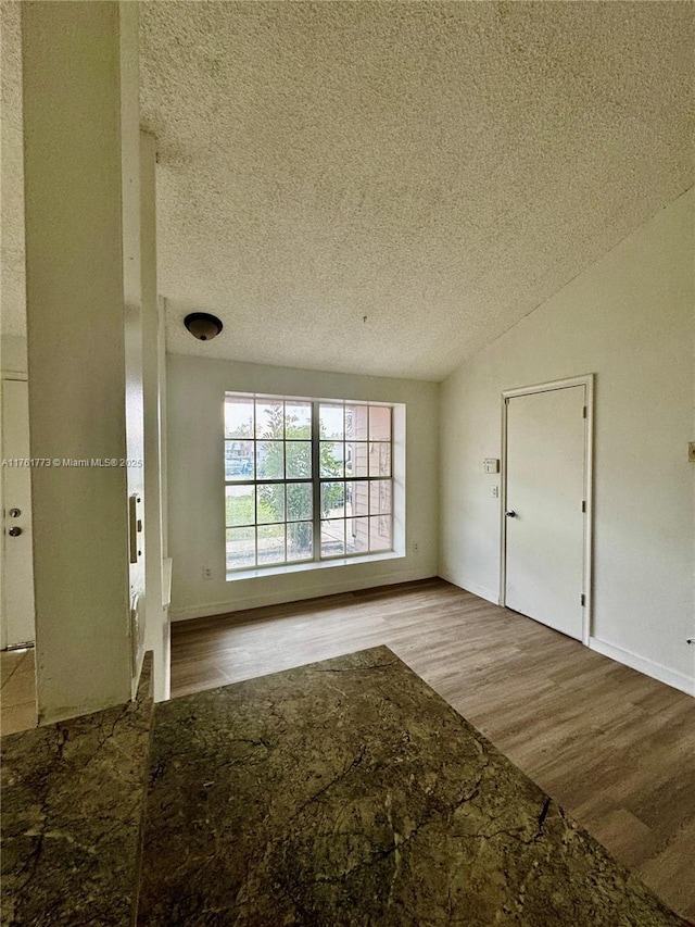 empty room with vaulted ceiling, wood finished floors, baseboards, and a textured ceiling