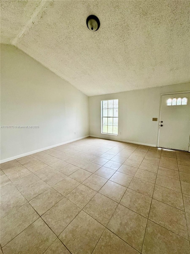 empty room featuring tile patterned floors, a textured ceiling, baseboards, and vaulted ceiling