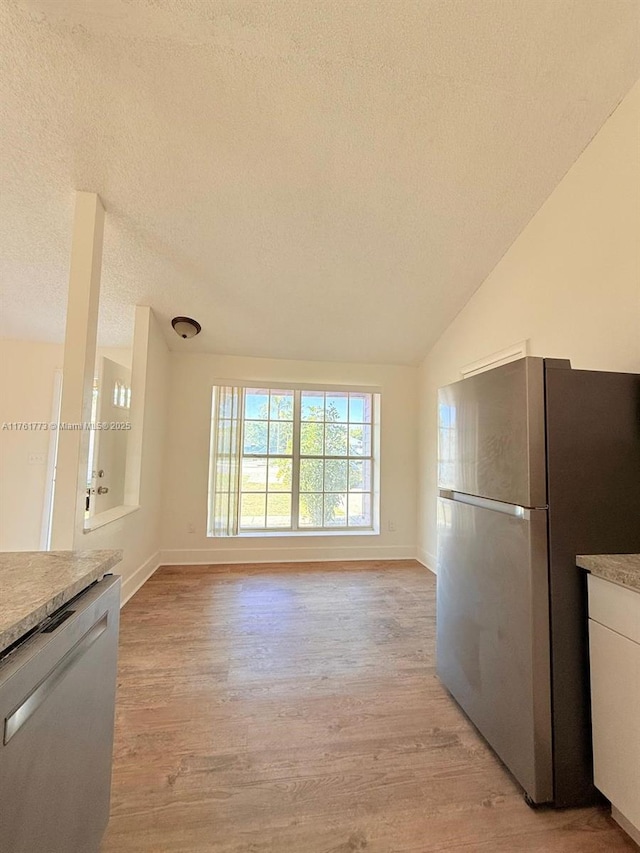 kitchen featuring light wood-type flooring, a textured ceiling, appliances with stainless steel finishes, and vaulted ceiling