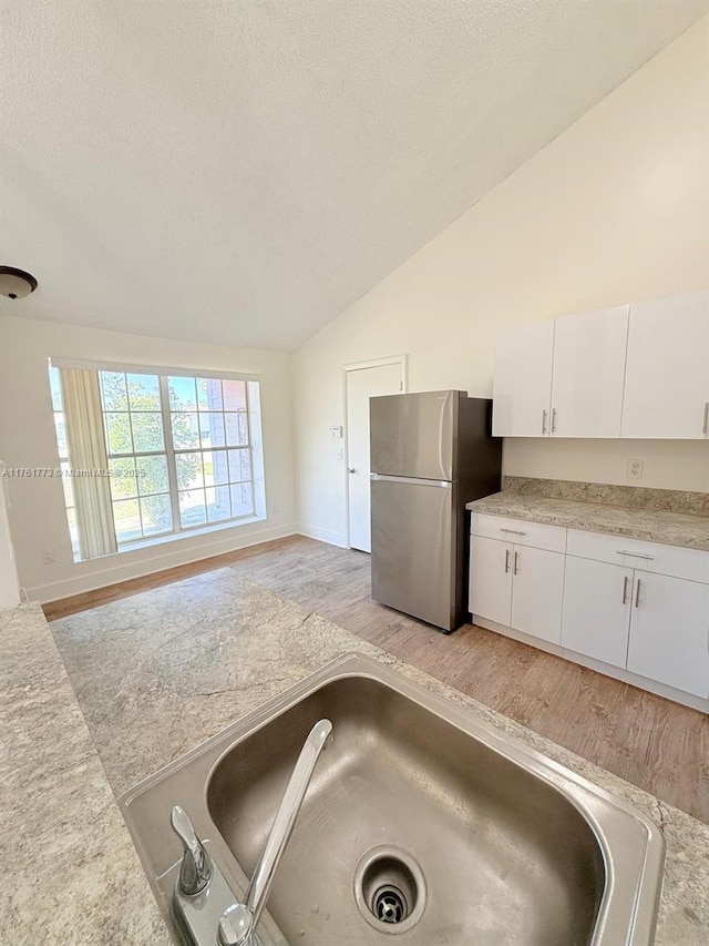 kitchen featuring lofted ceiling, freestanding refrigerator, a sink, light countertops, and white cabinets