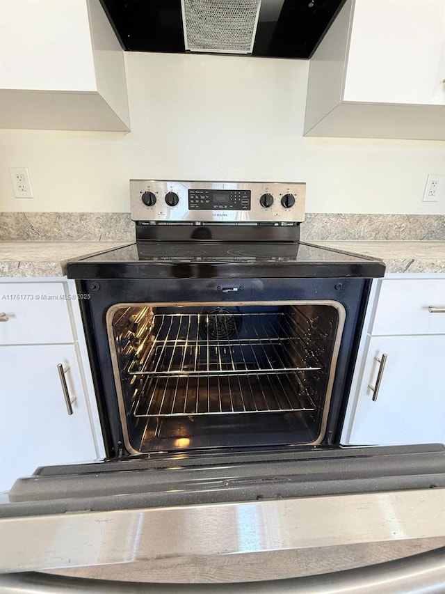 room details featuring light countertops, wall chimney range hood, stainless steel electric stove, and white cabinets