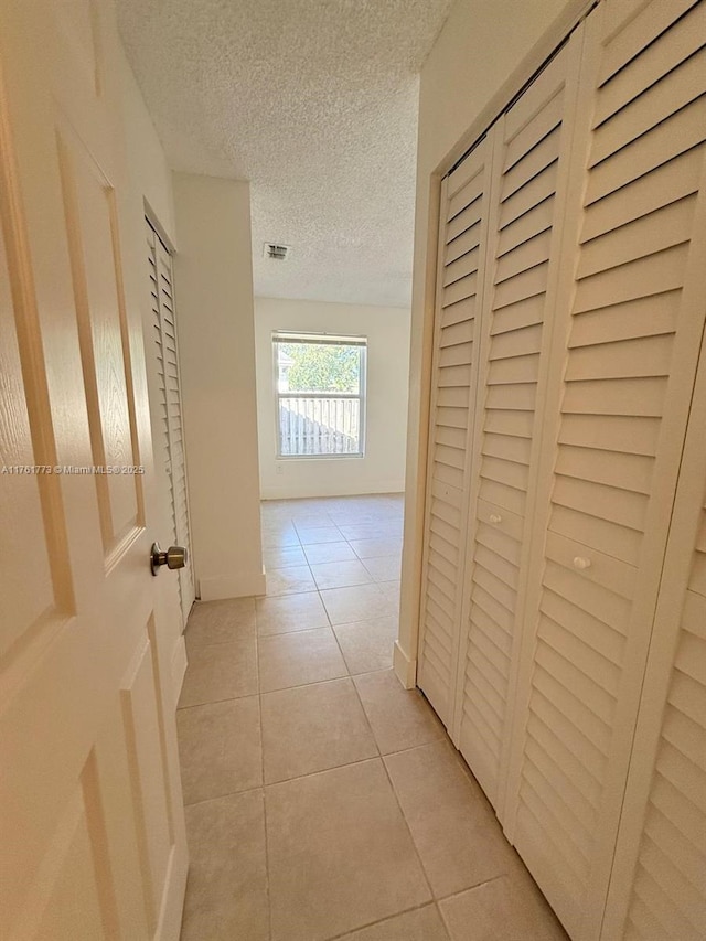 hallway with light tile patterned floors, visible vents, and a textured ceiling