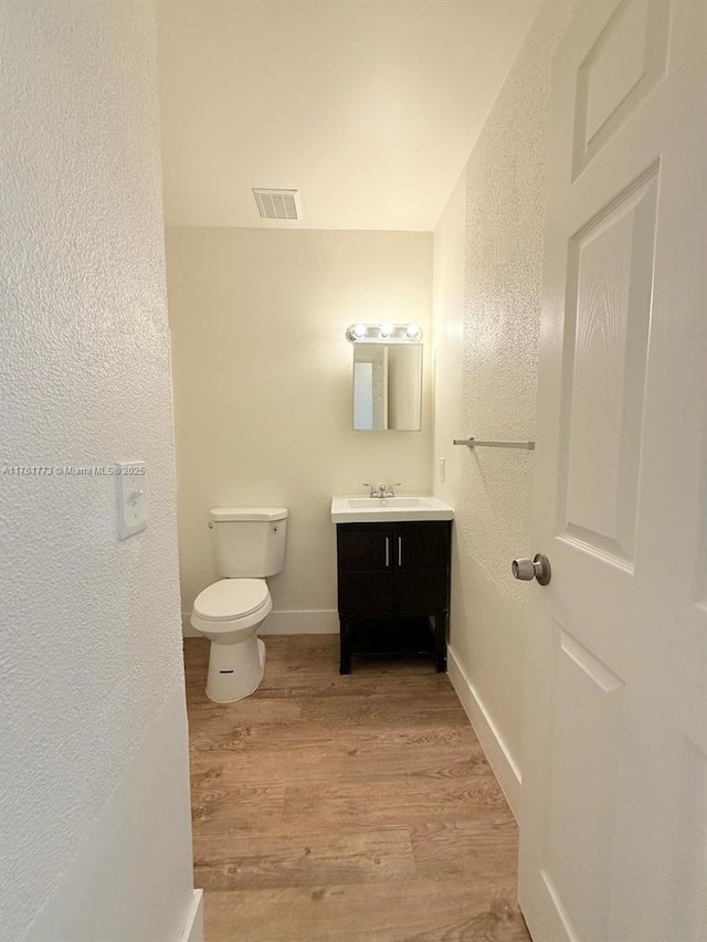 bathroom with vanity, wood finished floors, visible vents, baseboards, and toilet