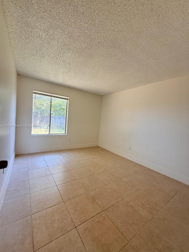 spare room featuring light tile patterned floors, a textured ceiling, and baseboards