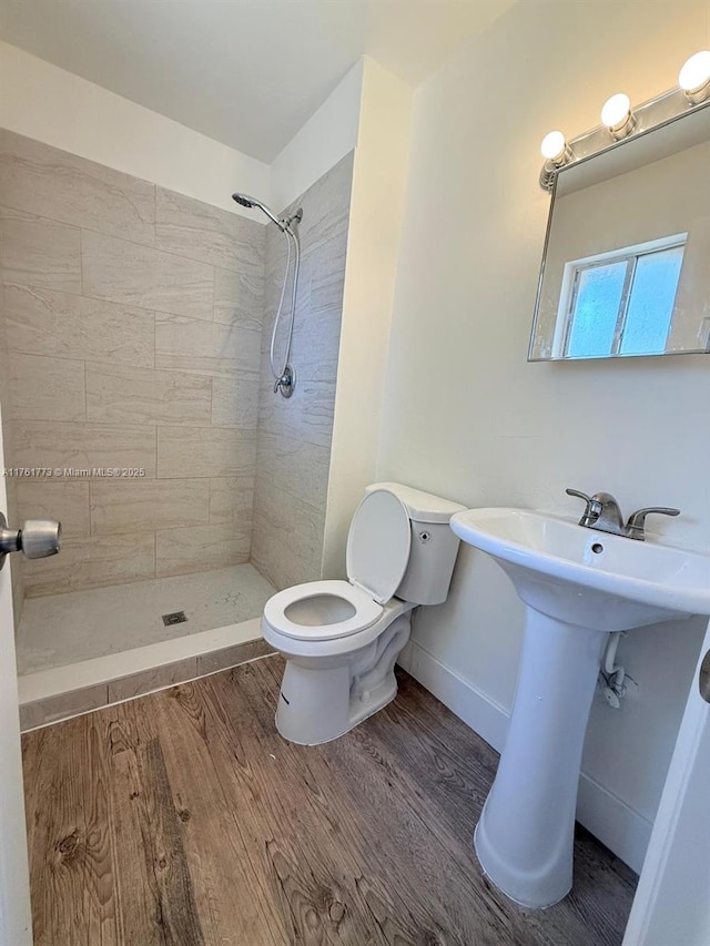 full bathroom with a tile shower, toilet, baseboards, and wood finished floors