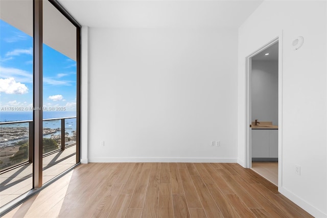 empty room with light wood finished floors, baseboards, a water view, a wall of windows, and a sink