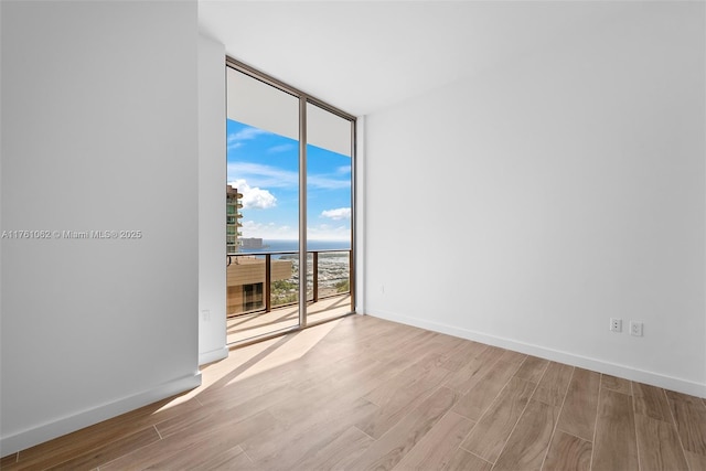 unfurnished room with a wall of windows, wood finished floors, and baseboards