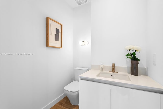 half bath featuring visible vents, toilet, wood finished floors, baseboards, and vanity