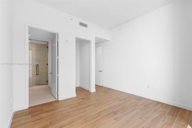 unfurnished bedroom featuring visible vents, baseboards, light wood-style floors, and ensuite bath