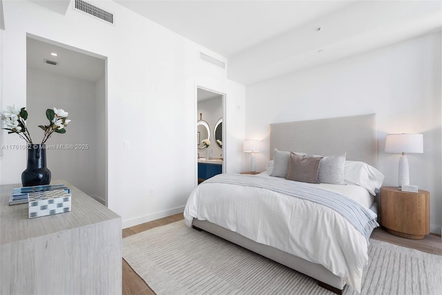 bedroom featuring connected bathroom, wood finished floors, visible vents, and baseboards