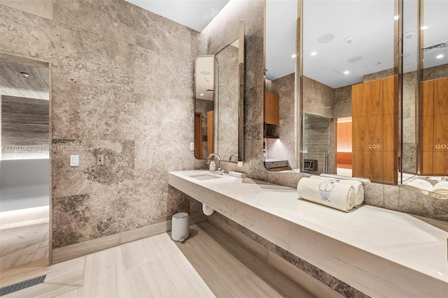 full bathroom with tile patterned flooring, tile walls, visible vents, and a sink