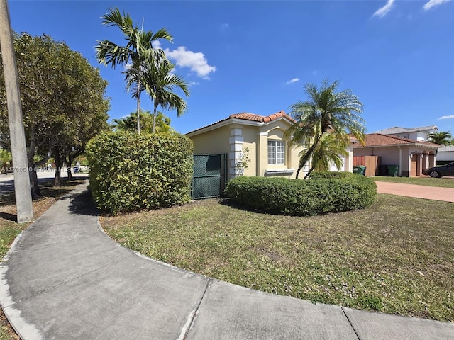 mediterranean / spanish house featuring a front lawn, a tile roof, stucco siding, driveway, and a gate