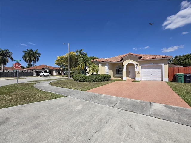 mediterranean / spanish home featuring fence, an attached garage, stucco siding, a tile roof, and decorative driveway