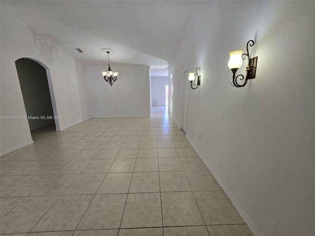 spare room featuring light tile patterned flooring, baseboards, arched walkways, and a chandelier