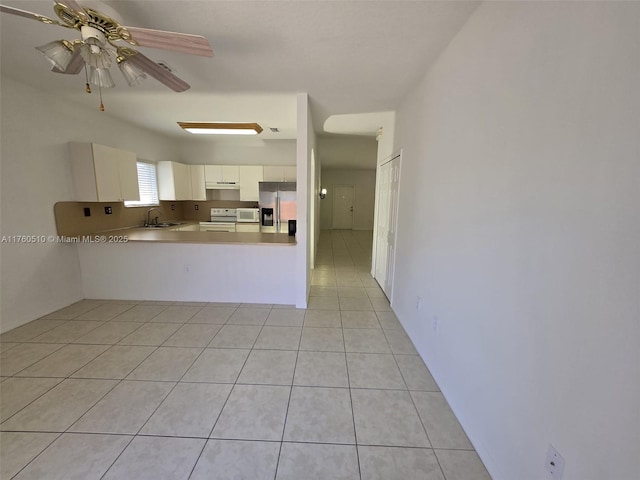 kitchen featuring light tile patterned floors, a sink, white cabinets, under cabinet range hood, and stainless steel fridge