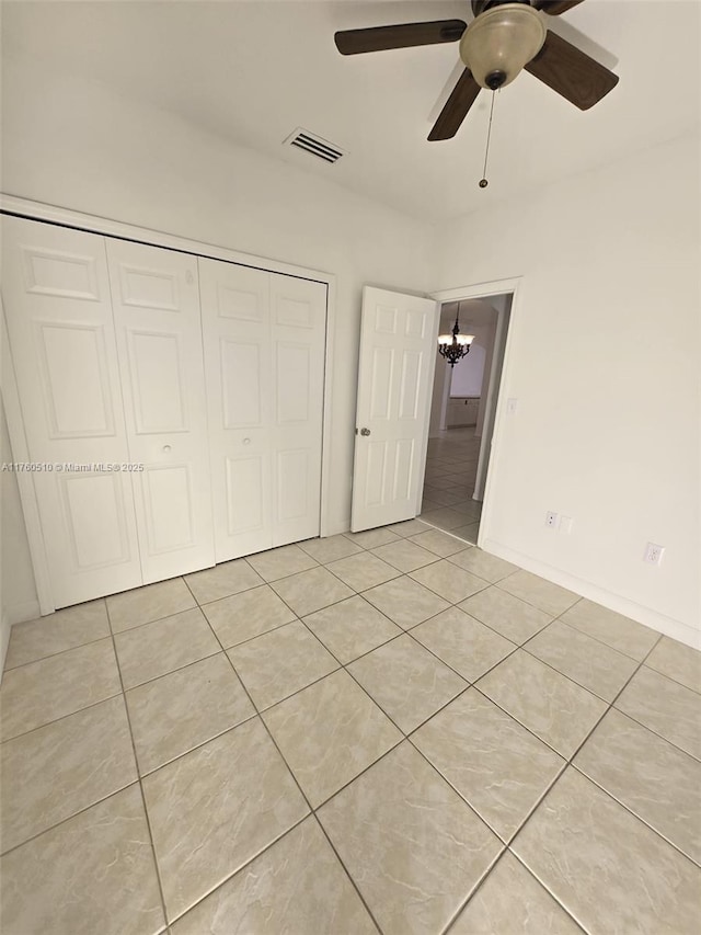 unfurnished bedroom with light tile patterned floors, visible vents, ceiling fan with notable chandelier, and a closet