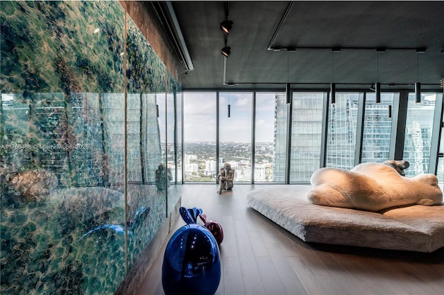 interior space with rail lighting, a view of city, expansive windows, and wood finished floors